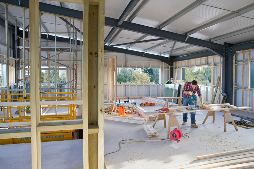 Construction site of a custom home blueprint, featuring a worker using a circular saw, surrounded by framing materials and tools, emphasizing the building process for tailored homes.
