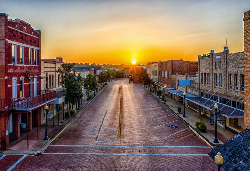 Historic downtown Nacogdoches at sunset, featuring red brick buildings, tree-lined streets, and warm golden light, symbolizing East Texas charm and community.