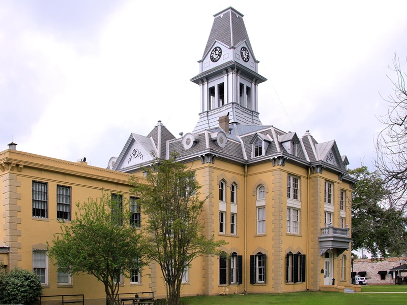 Historic yellow courthouse building with a clock tower, surrounded by greenery, representing architectural heritage in Newton County, TX.