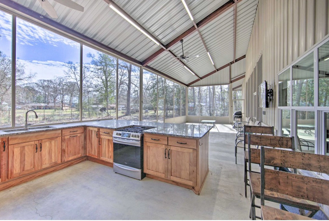 Barndominium patio kitchen with granite countertops, wooden cabinetry, and large windows overlooking a natural setting, showcasing an open design ideal for East Texas living.